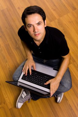 Young man sitting on the floor working on laptop computer at hom clipart