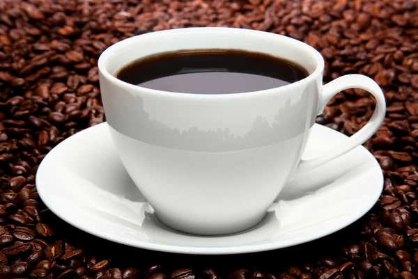 Xícara de café sentado em uma cama de grãos de café isolado sobre um backgr branco Fotografia De Stock