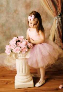 Adorable little girl dressed as a ballerina in a tutu standing next to pink roses. clipart