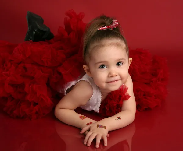 愛らしい少女の肖像画赤い服を着て赤い背景の上のバレンタインの日やクリスマス 彼女の腕に入れ墨をした偽 — ストック写真
