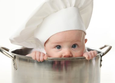 Close up portrait of a baby sitting wearing a chef hat sitting inside a large cooking stock pot, isolated on white clipart