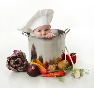 Portrait of a smiling baby sitting wearing a chef hat sitting inside a large cooking stock pot surrounded by vegetables and food, isolated on white clipart