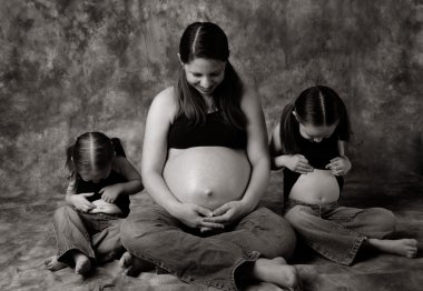 Maternity portrait of a pregnant mom and her two daughters all looking at their bellies clipart