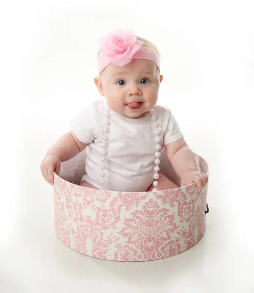 バラと白いシャツ 真珠のネックレスおよびピンクのヘッドバンドを着てピンクと白の Hatbox に座っているを突き出し舌の愛らしい赤ちゃんの肖像画 — ストック写真