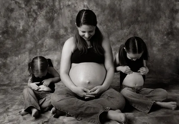妊娠中のお母さんと二人の娘たちは腹をすべて見ての産休の肖像 — ストック写真