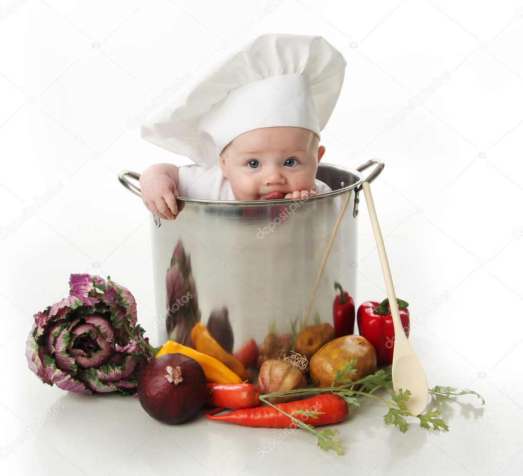 Portrait of a baby sitting wearing a chef hat sitting inside and licking a large cooking stock pot surrounded by vegetables and food, isolated on white