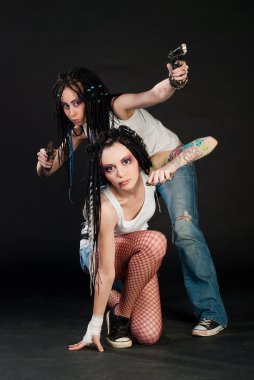 Two white girl with handguns on black background. One girl with body art on her hand. clipart