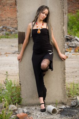 Fashionable girl in black dress alongside of column on the dirty industrial place clipart