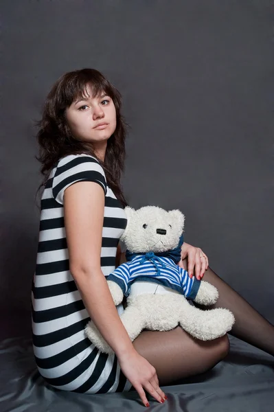 美女孩与玩具熊条纹穿灰色的背景上 — 图库照片
