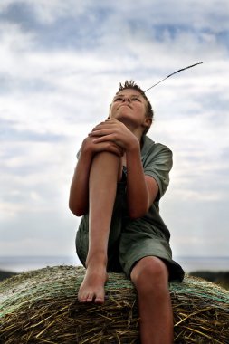 13 yaşında erkek bir balya saman yaz alanında üzerinde