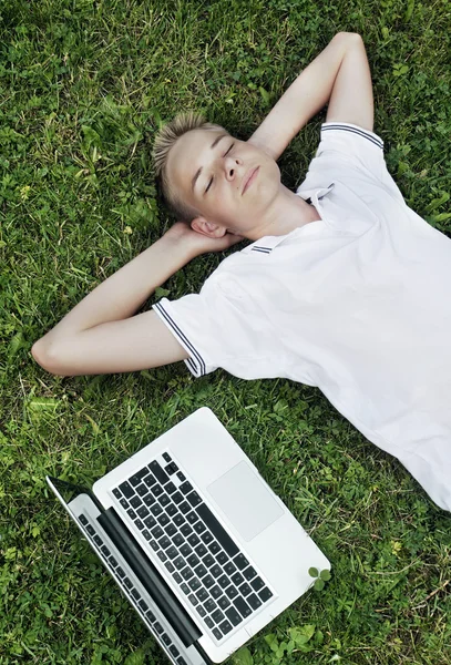 男孩拿着笔记本电脑躺在草地上 — 图库照片