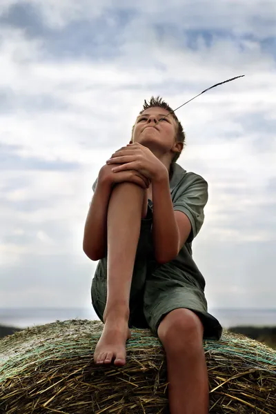 13 anni ragazzo su una balla di fieno in campo in estate — Foto Stock