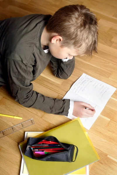 Rapaz a escrever no papel, deitado no chão — Fotografia de Stock