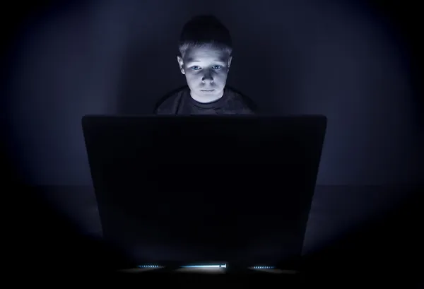 Menino iluminado pela luz azul de um monitor de computador — Fotografia de Stock