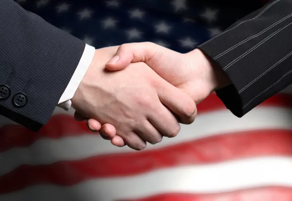 Händeschütteln und eine amerikanische Flagge im Hintergrund — Stockfoto
