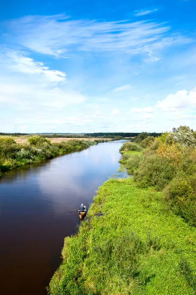 Blauwe rivier, wolk sky, groene oevers en kleine boot. — Stockfoto
