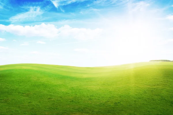 青い空で真昼の太陽の下で緑の芝生の丘. — ストック写真