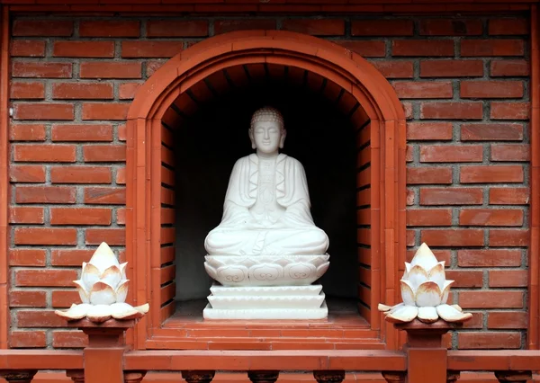 石の蓮のつぼみによって囲まれる寺院の壁のニッチに仏陀の坐像 — ストック写真