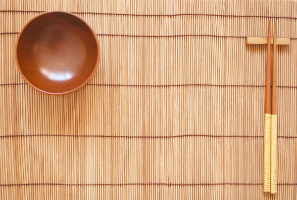 Pałeczki z drewniana miska na tle maty bambusowe — Zdjęcie stockowe