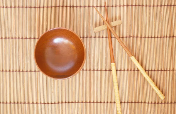 Palillos con tazón de madera sobre fondo de estera de bambú — Foto de Stock