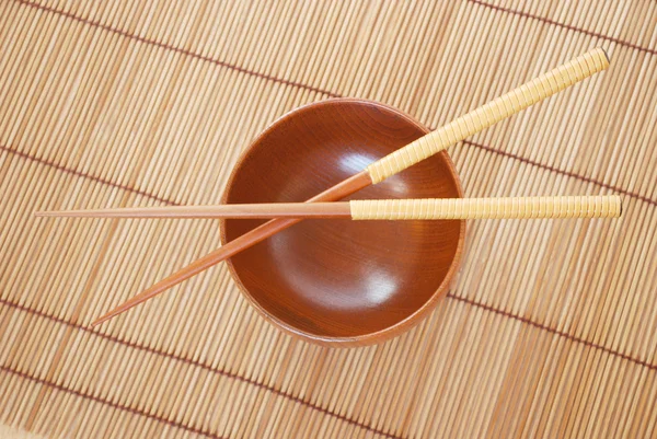 Chopsticks com tigela de madeira em fundo de esteiras de bambu — Fotografia de Stock