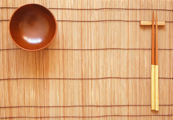 stock image Chopsticks with wooden bowl on bamboo matting background