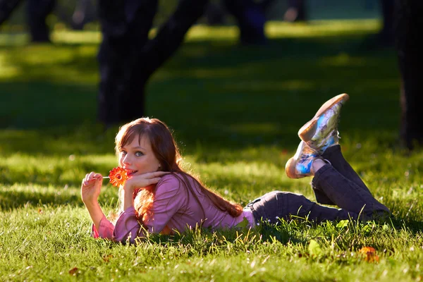 Beautiful girl licking candy in the park — Stock Photo, Image