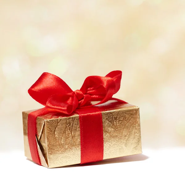 Scatola regalo dorata con fiocco rosso su sfondo sfocato — Foto Stock