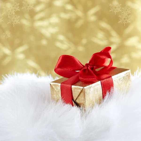Χρυσή δώρο κουτί με κόκκινη κορδέλα στη λευκή γούνα κατά τη χρυσή θαμπάδα — Φωτογραφία Αρχείου