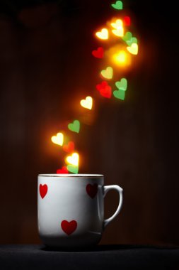 Cup with steam of glowing hearts on dark background clipart