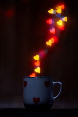 Cup emits steam of glowing hearts on dark background with copy space clipart