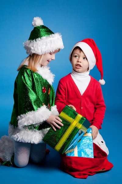 Девочка и мальчик в рождественских костюмах играют с подарками — стоковое фото