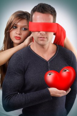 Woman blindfolding a man holding his open eyes heart in his hand clipart