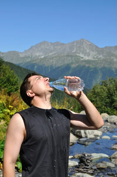 Молодий чоловік охоче п'є воду з пластикових пляшок — стокове фото