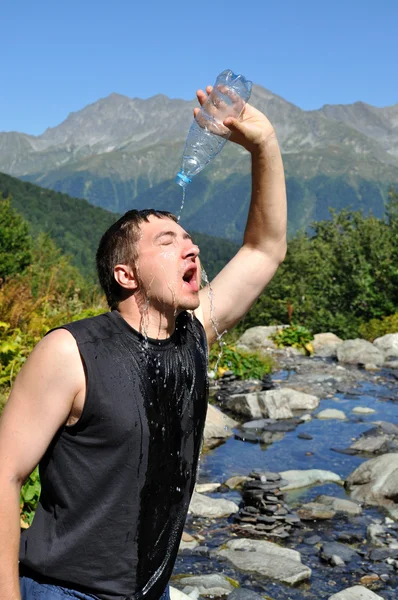 stock image A young man pours water on his head from a plastic bottle,