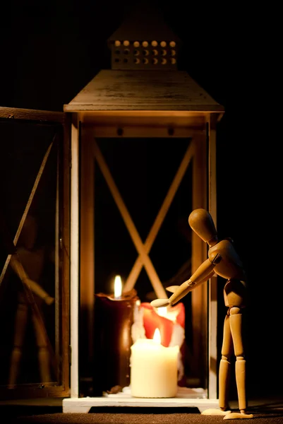 Una bambola snodata che si scalda su tre candele in una lanterna . Foto Stock Royalty Free