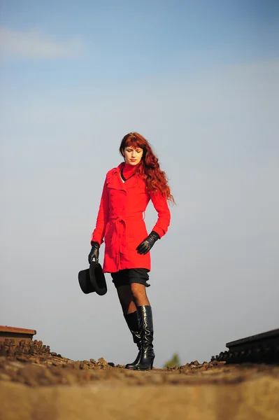 鮮やかな赤ジャケットの線路に行く若い赤髪の女 — ストック写真