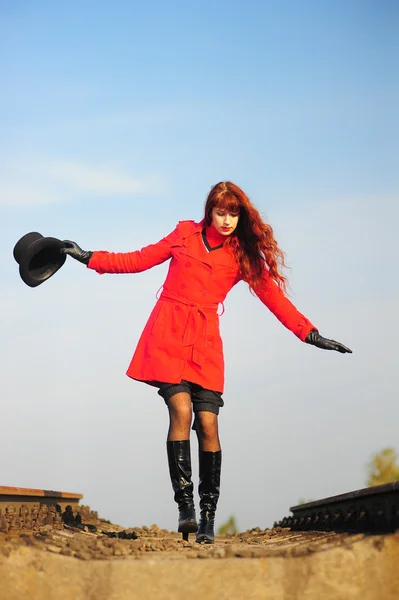 Stock image The young red-haired woman going on railroad tracks in brightly red jacket