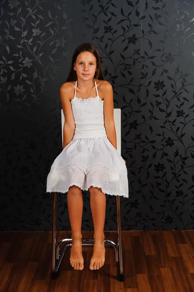 A menina de roupas brancas sentada em uma cadeira — Fotografia de Stock