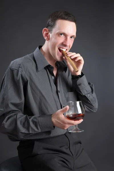 O cara com um charuto e conhaque em um fundo preto — Fotografia de Stock