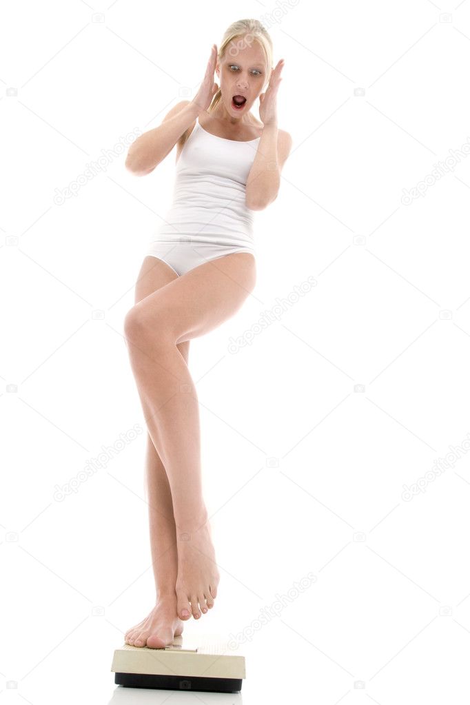 Young caucasian woman in underwear standing on weighing scales and scares