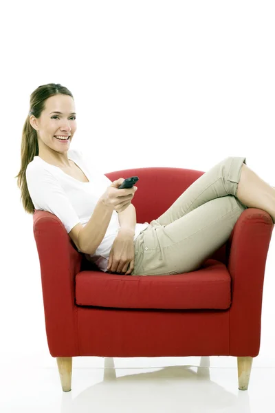 Jovem mulher sentada em uma cadeira com controle remoto no garanhão de fundo branco — Fotografia de Stock