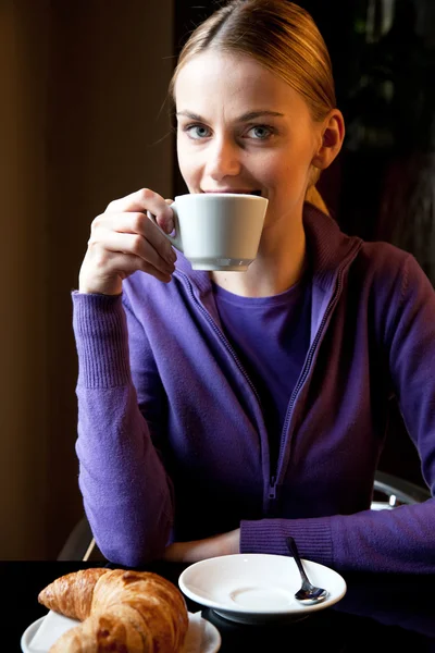 Nő iszik cappuccino reggeli és látszó-on fényképezőgép — Stock Fotó