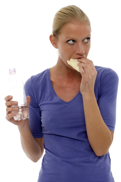 Portrait of a young caucasian woman holding a bottle of water and eating a — Stock Photo, Image
