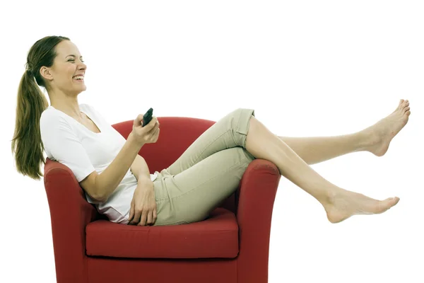 Giovane donna seduta su una sedia con telecomando su sfondo bianco st — Foto Stock