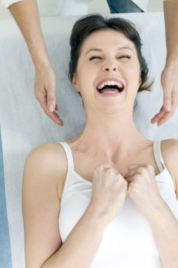 Young caucasian woman lying down smiling and receiving head massage clipart