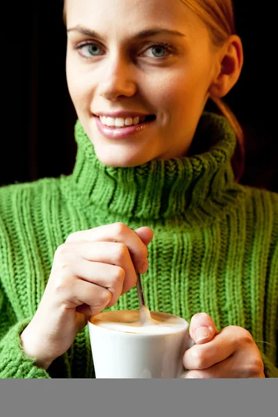 Jonge vrouw houdt een kopje cappuccino en camera te kijken — Stockfoto