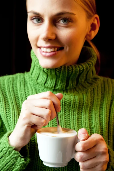 Young woman holding a cup of cappuccino and looking at camera — Stock Photo, Image