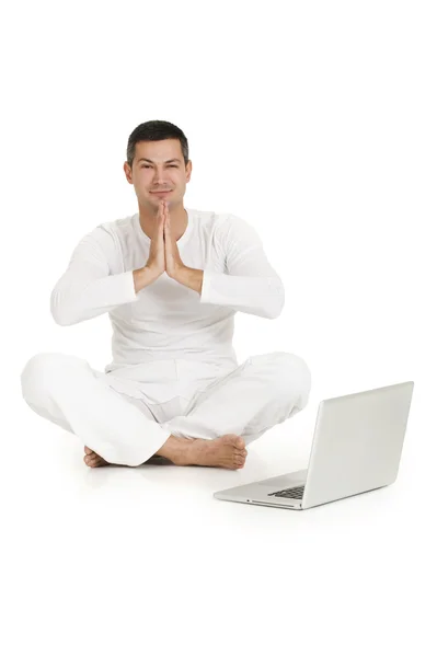 ชายที่แต่งตัวเป็นสีขาว นั่งอยู่บนพื้น ฝึกโยคะกับแล็ปท็อป — ภาพถ่ายสต็อก