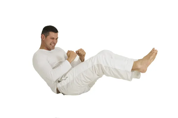 Man gekleed in witte zittend op de grond maakt de buik — Stockfoto